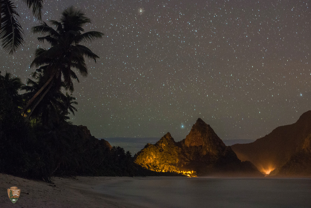Secluded Ofu sand beach at night. The island of Olosega rises in the distance at far right. Photo courtesy of the US National Park Service.