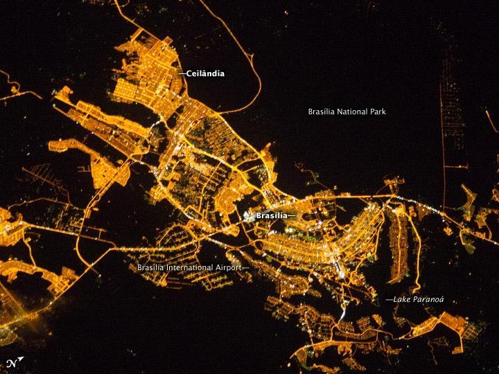 Whether seen at night or during the day, the capital city of Brazil is unmistakable from orbit. Brasilia is located on a plateau - the Planalto Central - in the west-central part of the country, and is widely considered to be one of the best examples of 20th century urban planning in the world. One of its most distinctive design features - as seen from above - suggests a bird, butterfly, or airplane traveling along a northwest-southeast direction, and is made dramatically visible by city light patterns (image center right, between Lake Paranoa and the airport). 
Following the establishment of Brasilia in the early 1960s, informal settlements began to form around the original planned city. Ceilandia was one such settlement. In 1970, Ceilandia was formalized by the government and is now a satellite city of Brasilia with its own distinct urban identity. The developed areas of Brasilia and its satellites are clearly outlined by street grids and highway lights in this photograph taken from the International Space Station. The large unlit region to the upper right is the Brasilia National Park. Image courtesy of NASA.