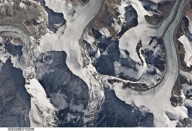 This detailed photograph taken from the International Space Station highlights the northern approach to Mount Everest from Tibet. Known as the northeast ridge route, climbers travel along the East Rongbuk Glacier (top right) to camp at the base of Changtse Mountain. From this point at approximately 6,100 m (20,000 ft) above sea level, the North Col - a sharp-edged pass carved by glaciers, center - is ascended to reach a series of progressively higher camps along the North Face of Everest, culminating in Camp VI at 8,230 m (27,000 ft) above sea level. Climbers make their final push to the summit (not visible, just off the bottom edge of the image) from this altitude. Image courtesy of NASA.


