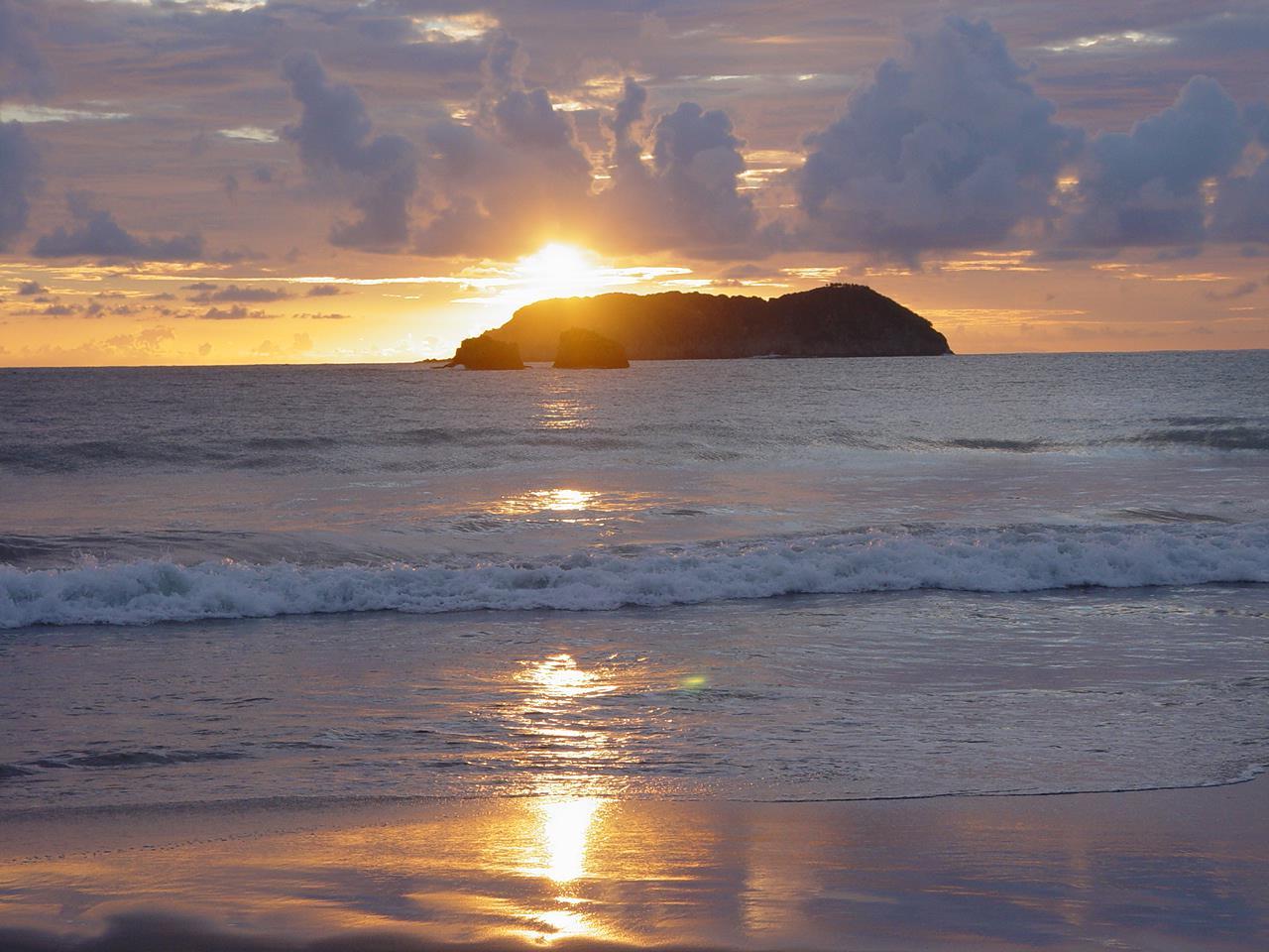 A sunset and its reflection create a golden sheen along a Costa Rican shoreline.