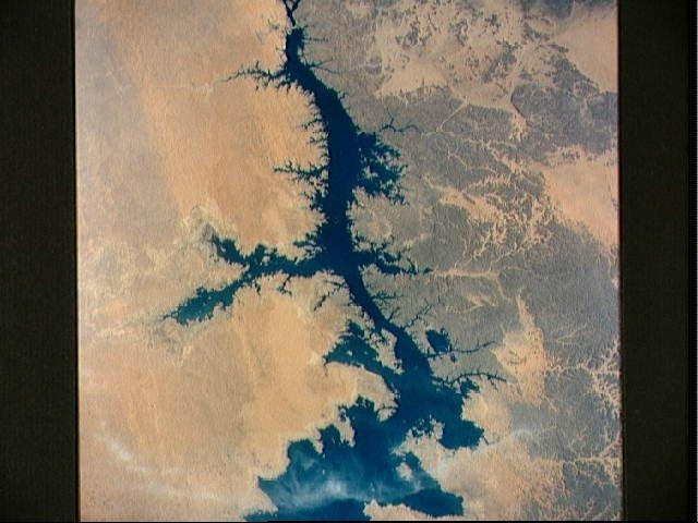 The Aswan High Dam (top of photo) is 4 km (2.5 mi) across and 111 m (364 ft) high. Completed in 1971, it was constructed to supply cheap hydroelectric power to both Egypt and Sudan by impounding, controlling, and regulating the flood waters of the Nile River in Lake Nasser, the world's second largest artificial lake. The lake extends over 800 km (500 mi) in length, covers an area of some 5,200 sq km (2,000 sq mi) and is as much as 107 m (350 ft) deep at the face of the dam. Click on photo for higher resolution. Image courtesy of NASA. 