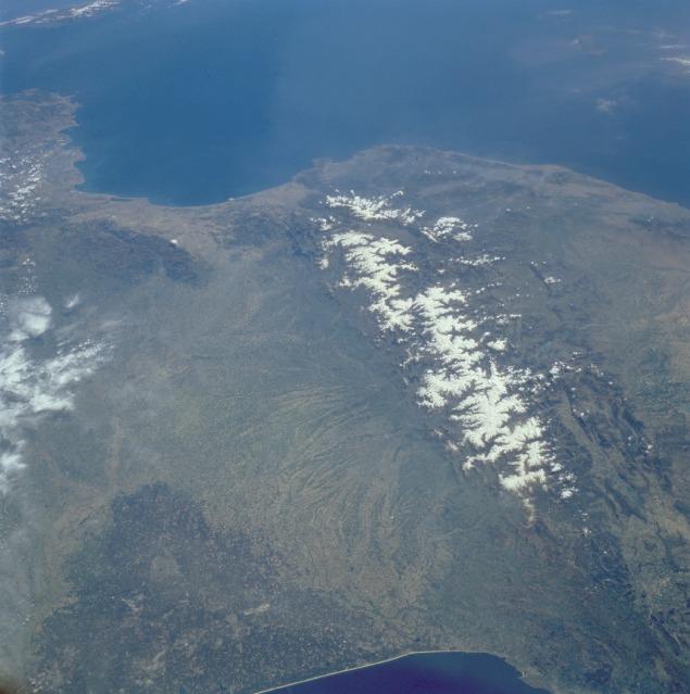 View of the Pyrenees Mountains between France and Spain taken April 1985. The snow-covered mountains, which form a formidable physical barrier between France to the north (left) and Spain to the south (right), are the main focus of this low-oblique, southeast-looking photograph. Scarcely interrupted by accessible passes and pierced in only two places by railroad tunnels, the Pyrenees are an ideal natural boundary between the Iberian Peninsula and the rest of Europe. The northern flank of the Pyrenees is characterized by a series of large alluvial deposits that fan out across southwestern France. The darker, roughly triangular area in southwest France is part of the forested Aquitaine Basin. The southern flank of the Pyrenees (Spain) is characterized by aridity and very rugged, mountainous conditions. Human settlement is sparse throughout the Pyrenees. However, because the region is rich in mineral waters, there are dozens of mineral water resorts, and winter sports attract visitors from southwestern France. The very small mountainous country of Andorra (not distinguishable in this photograph) has survived in an inaccessible upper valley of the Pyrenees. Image courtesy of NASA. 
