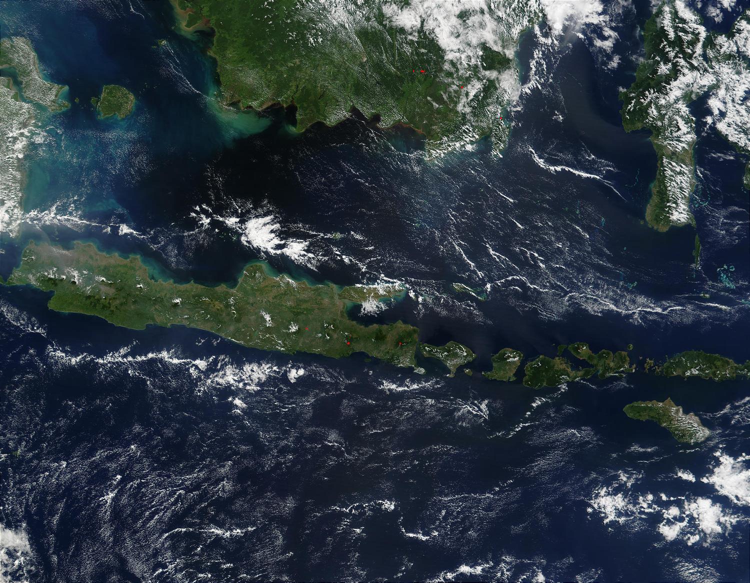 This true-color image of some of the Indonesian islands is from mid-May 2002. Fire season was not fully underway in the region, and skies over the large island of Borneo (top) were partially cloud-covered, but not hazy with air pollution. The horizontally situated island of Java appears to be experiencing some haze at its western end, and a few scattered fires (red dots) are apparent. Image courtesy of NASA.

