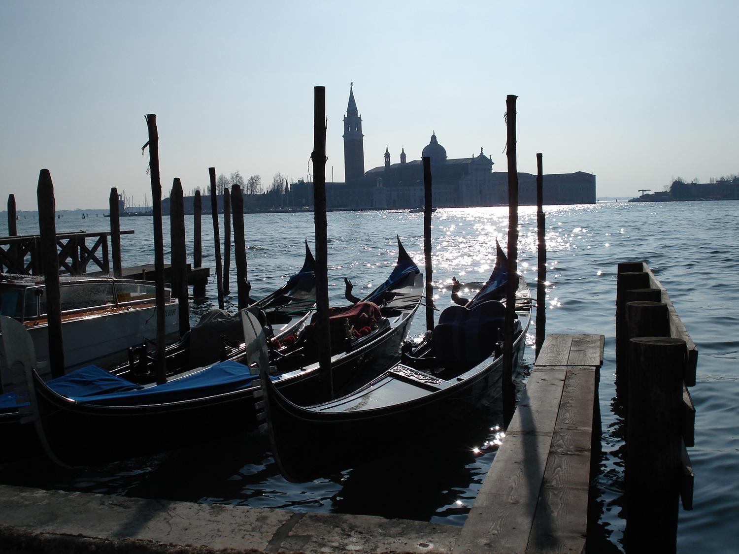 A view of San Giorgio Maggiore Island in Venice across the sparkling waters of the lagoon with gondolas in the foreground.