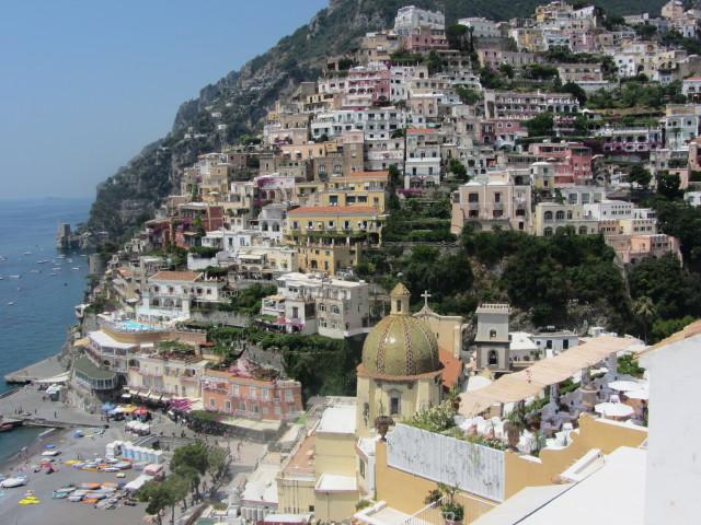  View of the city of Positano on the rugged Amalfi Coast showing the church Our Lady of the Assumption in the foreground and homes built vertically on a cliff in the background.
