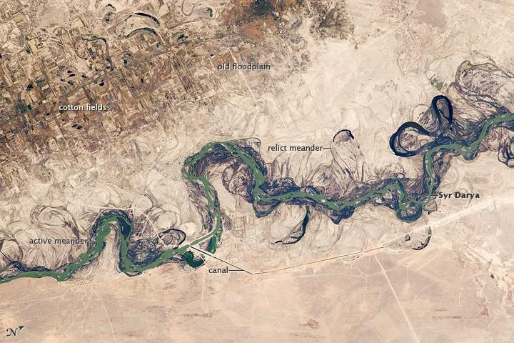 Central Asia's most important cotton-growing region is concentrated in the floodplain of the Syr Darya. The floodplain is shown here as a tangle of twisting meanders and loops (image center). The darkest areas are brushy vegetation along the present course (filled with blue-green water); wisps of vegetation are also visible along flanking swampy depressions, or sloughs. An older floodplain appears as more diffuse dark vegetation (image upper left), where relict bends are overlain by a rectangular pattern of cotton fields. The straight channel of a new diversion canal can be seen along the east bank of the river. Half the river flow is controlled from reservoirs, and half from direct water take-off from canals. In contrast to the intensive agricultural use of water shown here, water control in the mountain valleys upstream is oriented more toward power generation.
The river flows for 2,200 km (1,370 mi), from the Tien Shan Mountains west and northwest to the Aral Sea. Control of the river is vested in the Syr Darya Basin Water Organization, run by nations with territory in the watershed. Some of the organization's main efforts include accurate gauging of water use and repair of canals to reduce widespread water leakage. Photo courtesy of NASA.
