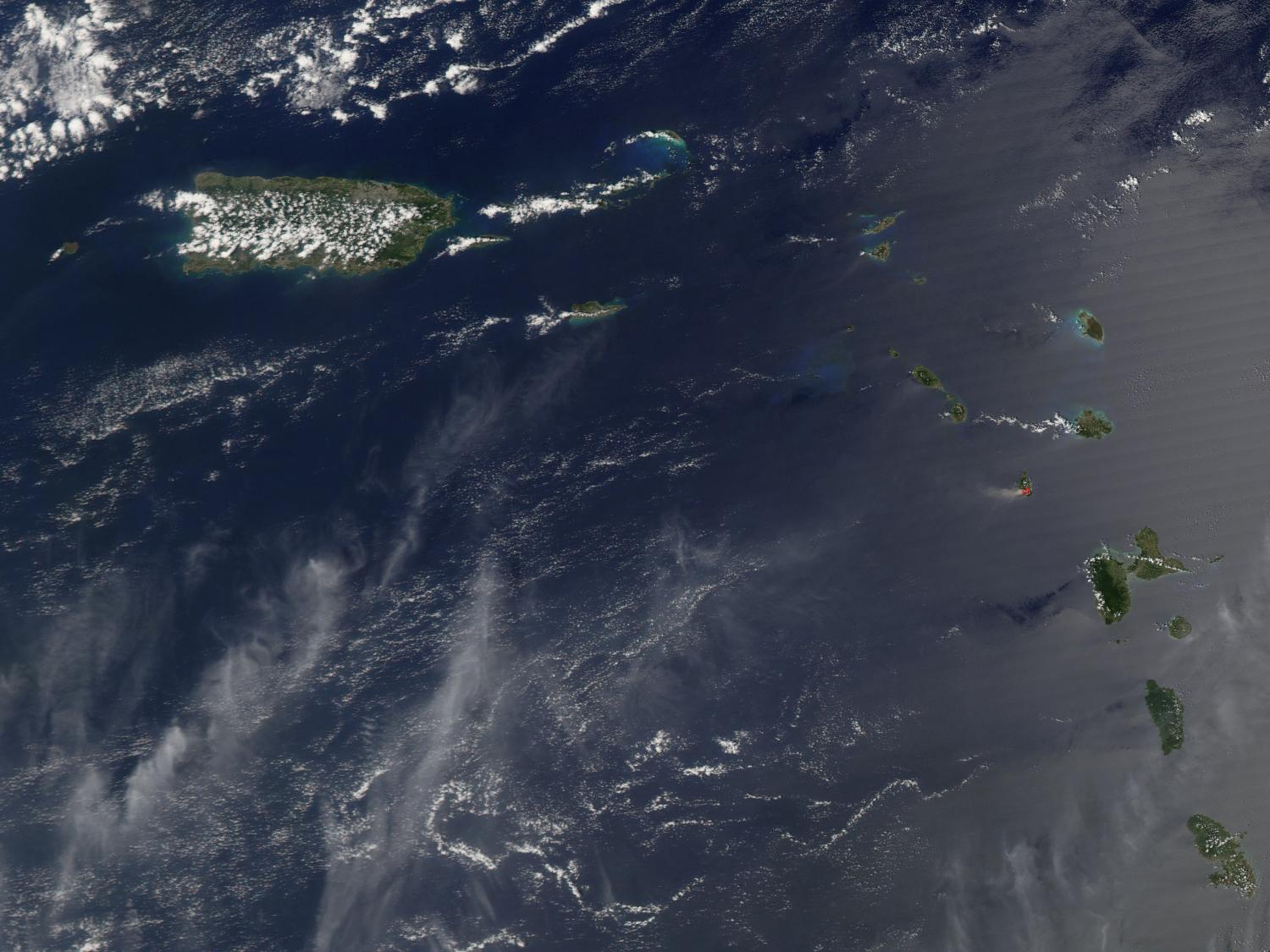 A view of Puerto Rico (upper left) and the isles of the Lesser Antilles. The Soufriere Hills Volcano on the island of Montserrat began emitting steam and ash on 9 February 2006. Low-level activity continued for several days. The volcano produced another plume on 20 March 2006, which is captured on this image. The volcano's pale beige ash plume blows westward over the Caribbean Sea. The red outline shows where the satellite detected a thermal anomaly, an area where the ground surface was significantly hotter than its surroundings. Image courtesy of NASA. 