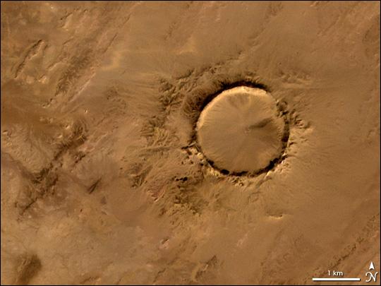 Deep in the Sahara lies a crater, a nearly a perfect circle that is 1.9 km (1.2 mi) wide, and sports a rim 100 m (330 ft) high. The Tenoumer crater sits in a vast plain of rocks so ancient they were deposited hundreds of millions of years before the first dinosaurs walked the Earth. Close examination of the structure has revealed that the crater's hardened "lava" was actually rock that had melted from a meteorite impact.

On this satellite image the crater&amp;apos;s outline is unmistakable, yet it does not necessarily look like a crater; the light and shadows make it look more as if someone pressed a giant cookie cutter into the rock. In this image, the sunlight shines from the southeast (lower right), and the bright arc along the northwestern part of the crater is where the crater walls slope up to the rim. Around the perimeter, the relatively steep walls cast dark shadows. Although it resides in ancient rock, Tenoumer is geologically young, ranging in age between roughly 10,000 and 30,000 years old. Photo courtesy of NASA.