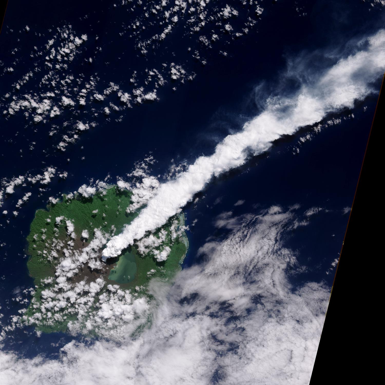 The thick, steam-rich plume from Guau Volcano blows directly northeast in this natural-color satellite image acquired on 24 April 2010. The thick steam is brighter white than the surrounding lower-altitude clouds. Vegetation is green, as is Lake Letas. Vegetation to the south and west of the volcano, damaged by ash and acidic volcanic gases, is dark gray-brown. Photo courtesy of NASA. 