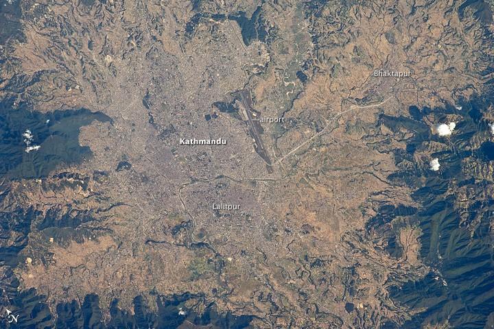 The capital and largest city of Nepal, Kathmandu, occupies much of the valley located near the center of the country. Nepal is home to much of the Himalaya mountain range between Tibet (China) to the north and India to the south. Geological and fossil evidence indicates that the Kathmandu Valley was covered by a large lake between approximately 2.8 million and 10,000 years ago. Paleo-Kathmandu Lake is thought to have drained in phases due to the drying of the regional climate; continuing mountain building-tectonic uplift and faulting-in the region; and the formation of an integrated drainage system, as river channels cut through previous rock ridge dams.
The green, vegetated slopes that ring the Kathmandu metro area (light gray, image center) include both forest reserves and national parks. The metropolitan area is relatively flat compared to the surrounding mountains. Tribhuvan International Airport, near the eastern margin of the city, is the only international airport in Nepal. 
Archeological evidence suggests that the human development of Kathmandu, together with the nearby "sister cities" of Lalitpur and Bhaktapur, began almost 2,000 years ago. Today, the three cities form the governmental, cultural, and-as a main access point to the Himalayas for tourism-economic center of the country. Photo courtesy of NASA.