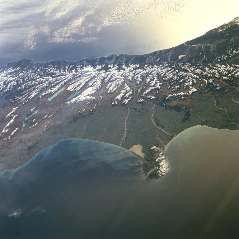 A westward-looking view of central South Island, showing the snow-covered Southern Alps fronted by the Canterbury Plain, the largest area of fertile, flat land in New Zealand. Running southwest to northeast along the western coast of South Island, the Southern Alps are rugged mountains made up of numerous peaks in excess of 3,000 m (9,840 ft). Within the Southern Alps, there are over 3,100 active glaciers. Click on photo to increase resolution. Image courtesy of NASA.