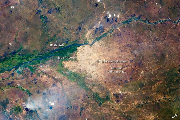 Juba, a port city on the White Nile, is the capital of South Sudan and one of the fastest growing cities in the world. Juba's population is estimated to be roughly 350,000 to 400,000. The city has doubled in size since 2005, when a peace agreement ended the civil war in Sudan. Both hopeful immigrants and returning residents have created the population surge. The city was a central point for humanitarian aid, and the operations base for the UN and NGOs during the Sudanese conflicts. During the fighting, city infrastructure and main transportation arteries suffered heavy damage. The city is still surrounded by army camps and squatter settlements (labeled "informal built-up areas" in the image). They appear as muted gray areas extending outward from the center of the city. The city also hosts the Juba Game Reserve, a protected area of savannah and woodlands that is home to key bird species. Since independence, a variety of countries and international organizations have helped rebuild Juba's roads, railroads, and airport. Unfortunately, South Sudan continues to experience local wars with a variety of armed groups, including on-going conflicts with Sudan over oil-rich territories. Image courtesy of NASA.