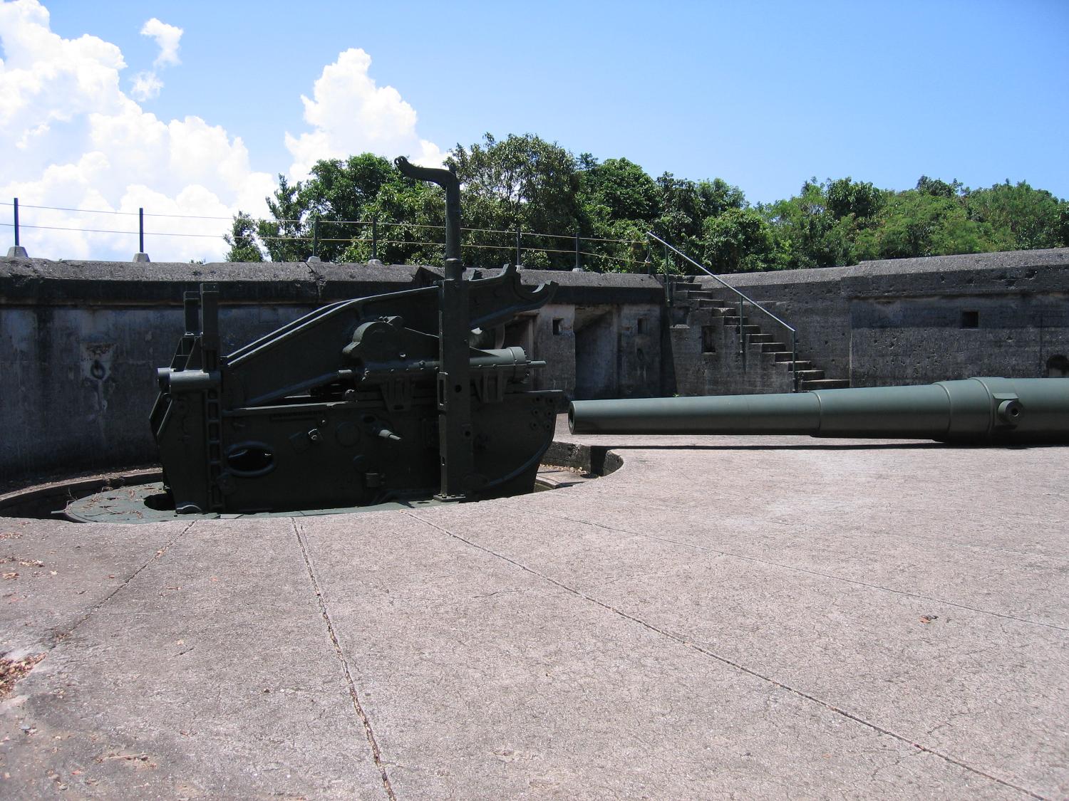 A 10-inch coast artillery gun and a "disappearing" mount emplaced in Battery Grubbs on Fort Mills (Corregidor). This type of mount is designed to employ a hinged counterweight to raise the gun for firing above the parapet of the gun emplacement and then to recoil back and down under cover for reloading. Fort Mills had 23 batteries with 56 coast artillery guns and mortars, of which six batteries were equipped with disappearing mounts. In addition, there were 13 anti-aircraft batteries with 76 guns.