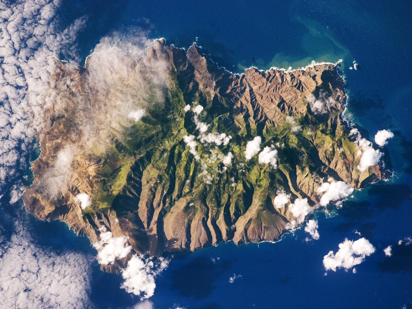 Saint Helena's rugged topography of sharp peaks and deep ravines - evident in this photograph from the International Space Station - is the result of erosion of the volcanic rocks that make up the island. A climatic gradient related to elevation is also evident - the higher, wetter central portion of the island is covered with green vegetation, whereas the lower coastal areas are drier and hotter with little vegetation cover. Image courtesy of NASA.  