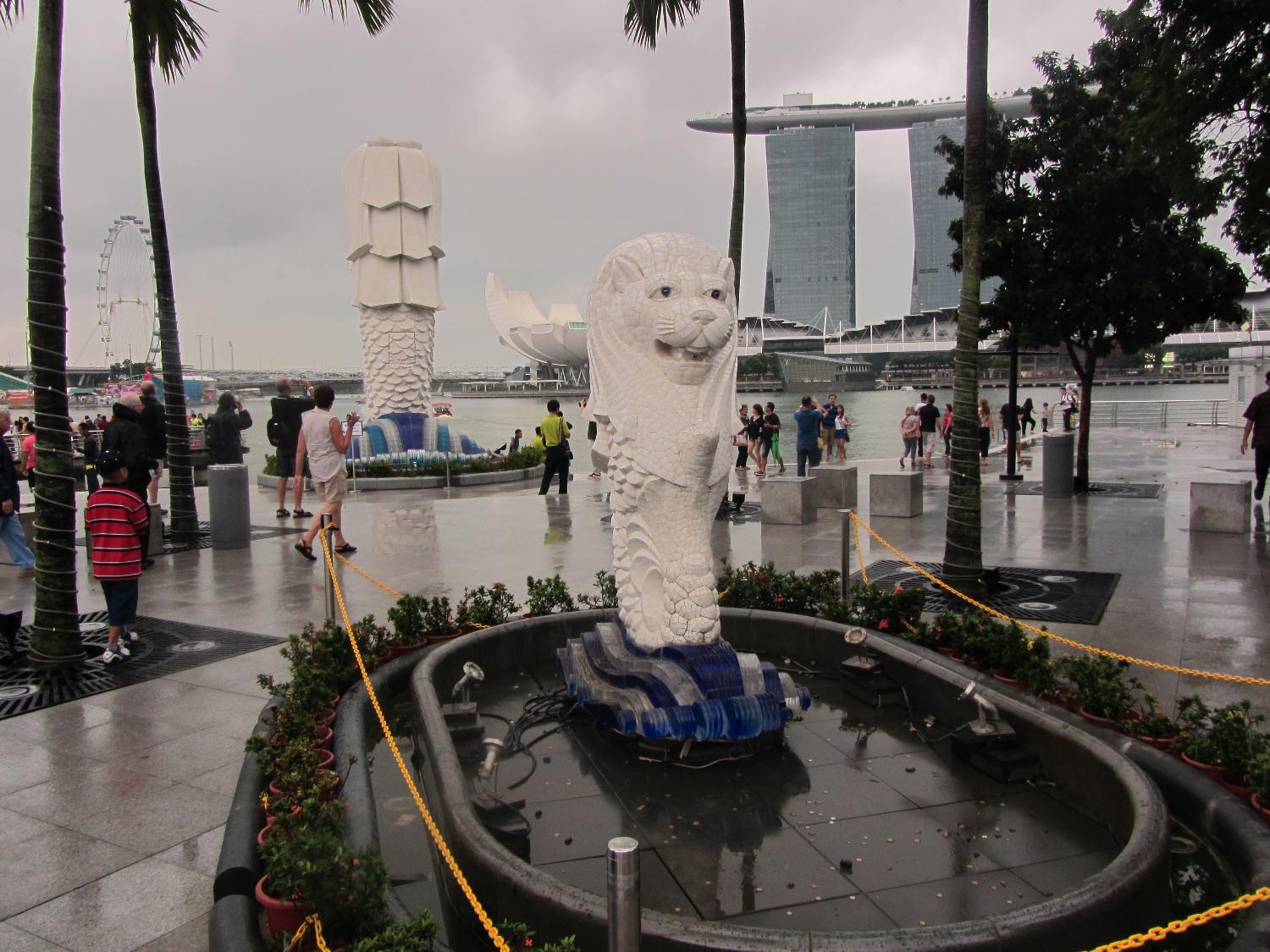 Smaller of the two Merlions (lion head and body of a fish) along the Singapore River. The word "Sing" comes from the Malay word for lion; thus the city is often called "Lion City." In the background looms the back of the statue of the larger Merlion, the Marina Bay Sands Hotel built to resemble a ship on towers, and the lotus flower-shaped ArtScience Museum.