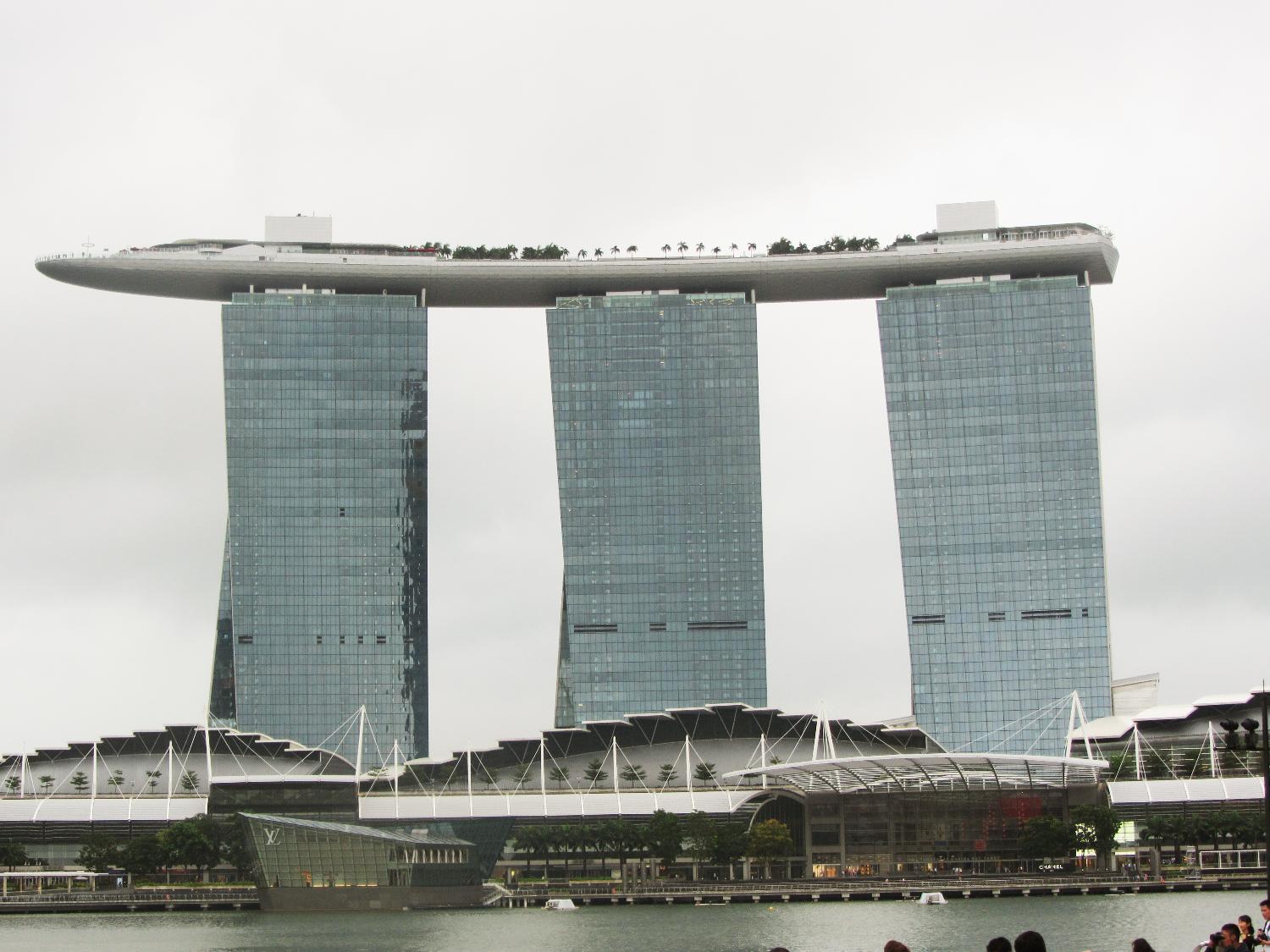 View of the Marina Bay Sands complex in Singapore that opened in 2010 and has since become a city landmark. The three 55-story towers contain hotel rooms. The upper level Sky Park, built to resemble a ship, has the world's longest elevated swimming pool, restaurants, gardens, and a public observation deck. The integrated resort also includes an adjacent ArtScience Museum, a casino, and a convention center.