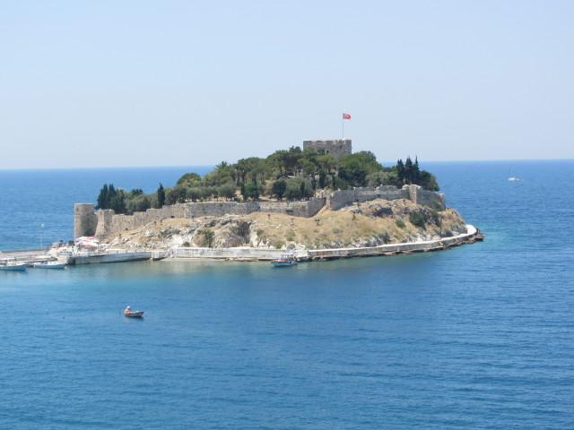 Pigeon Island (Guvercin Adasi) in the harbor of Kusadasi. The island is connected to the mainland by a causeway. The fortress dates from the 14th and 15th centuries. In 1834, the castle was rebuilt and the garrison expanded. The island became the focus of the town to the extent that people began referring to the whole town as Kusadasi (Bird Island).  


