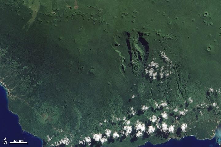 At the western end of the Samoan Island chain lies Savai'i. Stretching over 1,682 sq km (649 sq mi), Savai'i is one of the largest landmasses in Polynesia. The mountainous island is a shield volcano that reaches its highest altitude, 1,858 m (6,095 ft), near the center of the island. The region's tropical, humid climate sustains vegetation that carpets much of the island.
A jagged line of small, round volcanic craters extends east-west across the island (top of image). South of this uneven line, two deep, parallel valleys extend toward the south. The semicircular contours of the valleys suggest that they might be the remains of an ancient caldera or collapsed magma chamber that was modified by the later eruption of additional lava.
With the exception of a few brown crater rims, and a coastal settlement along the image's left edge, the landscape appears in varying shades of green. Dense rainforests cover the island's rugged interior, and thick vegetation also thrives along the coastal plains. 
Savai'i has remained volcanically active into historical times, with two eruptions occurring in the early 20th century. The eruptions sent big lava flows to the island's northern coast, destroying several villages. Photo courtesy of NASA.