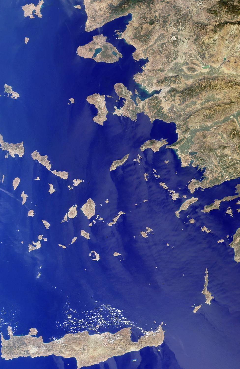 This image includes many of the islands of the East Aegean as well as part of mainland Turkey. The largest modern city in the Aegean coast is Izmir, Turkey, situated about one quarter of the image length from the top. The city is the bright coastal area near the greenish waters of Izmir Bay and southeast of the roughly triangular-shaped island of Lesvos. The lengthy island at the bottom of the photo is Crete. North of Crete, the small broken ring of islands are the remnants of the collapsed caldera of Santorini Volcano. Image courtesy of NASA. 