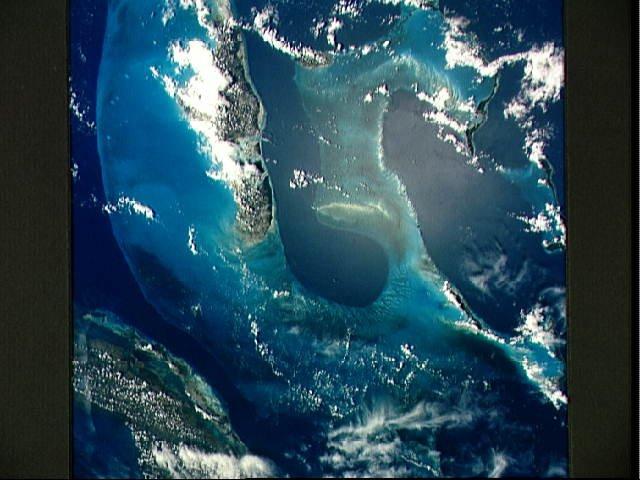 Most of the Western Bahama Banks, the Tongue of the Ocean (center), and Andros Island (left), as well as north central Cuba (lower left) with its fringing reefs, may be seen in this one view. The green-turquoise water over the banks is less than 9 m (30 ft) deep but the deep blue of the Tongue is 1,200 to 1,800 m (4,000 to 6,000 ft) deep. All the sediment on the banks, including the material that forms the islands, is calcium carbonate (lime) precipitated from sea water by animals and plants. Image courtesy of NASA. 
