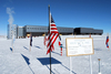 The Amundsen-Scott South Pole Station in the background, the ceremonial South Pole (candy stripe) in the center, and the actual geographic South Pole in the right foreground. Image courtesy of the National Science Foundation.