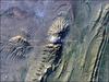 The Zagros Mountains in southwestern Iran present an impressive landscape of long linear ridges and valleys. Formed by collision of the Eurasian and Arabian tectonic plates, the ridges and valleys extend hundreds of kilometers. This astronaut photograph of the southwestern edge of the Zagros mountain belt includes another common feature of the region - a salt dome (Kuh-e-Namak or "mountain of salt" in Farsi). Thick layers of minerals such as halite (table salt) typically accumulate in closed basins during alternating wet and dry climatic conditions. Over geologic time, these layers of salt are buried under younger layers of rock. The pressure from overlying rock layers causes the lower-density salt to flow upwards, bending the overlying rock layers and creating a dome-like structure. Erosion has spectacularly revealed the uplifted tan and brown rock layers surrounding the white Kuh-e-Namak to the northwest and southeast (center of image). Radial drainage patterns indicate another salt dome is located to the southwest (image left center). If the rising plug of salt (called a salt diapir) breaches the surface, it can become a flowing salt glacier. Salt domes are an important target for oil exploration, as the impermeable salt frequently traps petroleum beneath other rock layers. Image courtesy of NASA.