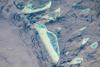 This photograph features one of the numerous atolls in the Maldive Islands chain. The Maldives are an island nation comprised of twenty-six atolls that stretch in a north-south chain for almost 900 km (560 mi) southwest of India. The silvery, almost pink sheen on the normally blue water of the equatorial Indian Ocean in the image is the result of sunglint, which is sunlight reflecting off of water surface directly back towards the observer. The largest island (image center) is 6 km (4 mi) long, and it is part of the 70-km-(40-mi-) long oval-shaped Male Atoll. Shores facing deeper water have well-defined beaches. Numerous small, elliptical coral reef islets are protected within the ring of shallow water to the northeast (image right). These islets are mostly awash at high tide. Image courtesy of NASA.
