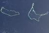 Majuro and Arno Atolls appear as meandering lines of delicate white against a darker ocean background in this satellite image. Areas of shallow water near the shore appear iridescent blue, especially in the southwest portion of each atoll and off the northwest tip of Arno Atoll. Overhead, tiny white clouds dot the sky. Majuro Atoll is 40 km (25 mi) in circumference, and it partially encloses a lagoon of nearly 300 sq km (115 sq mi). The lagoon is far bigger than the atoll itself, whose land area is less than 10 sq km (4 sq mi); walking from the lagoon side to the ocean side of the atoll takes only minutes. Neighboring Arno Atoll encloses three lagoons: two "pinched lagoons" in the northeast and northwest, and a main lagoon of nearly 340 sq km (130 sq mi). Arno's total land area is just 13 sq km (5 sq mi). Scientists have long understood that coral atolls develop around volcanic islands and remain there after those islands have eroded away. To what extent the final shape of an atoll is influenced by wind and ocean wave activity, however, remains a topic of debate. Image courtesy of NASA.